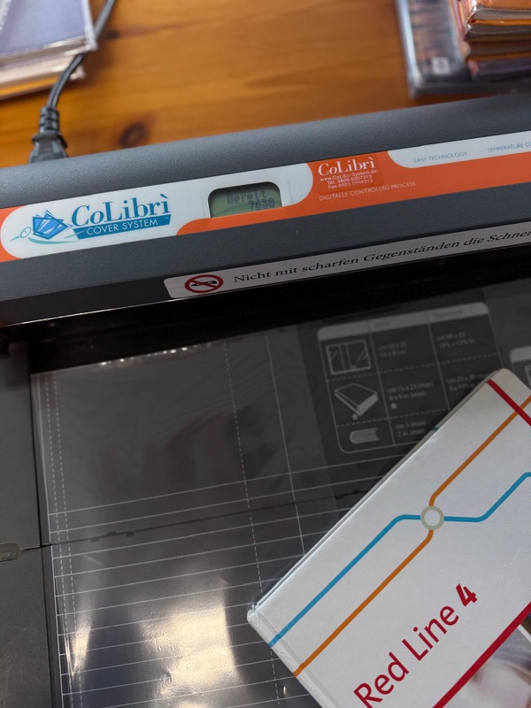 Ein fertig eingebundenes Schulbuch mit Schutzfolie neben dem CoLibrì-System
